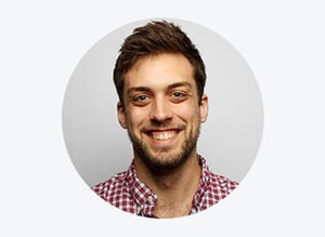 Erick Jorgensen in red and white checkered shirt smiling before a gray background.