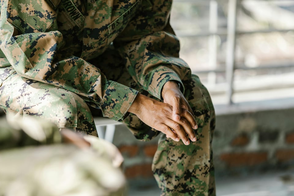 Person in a camouflage military uniform sitting with hands clasped