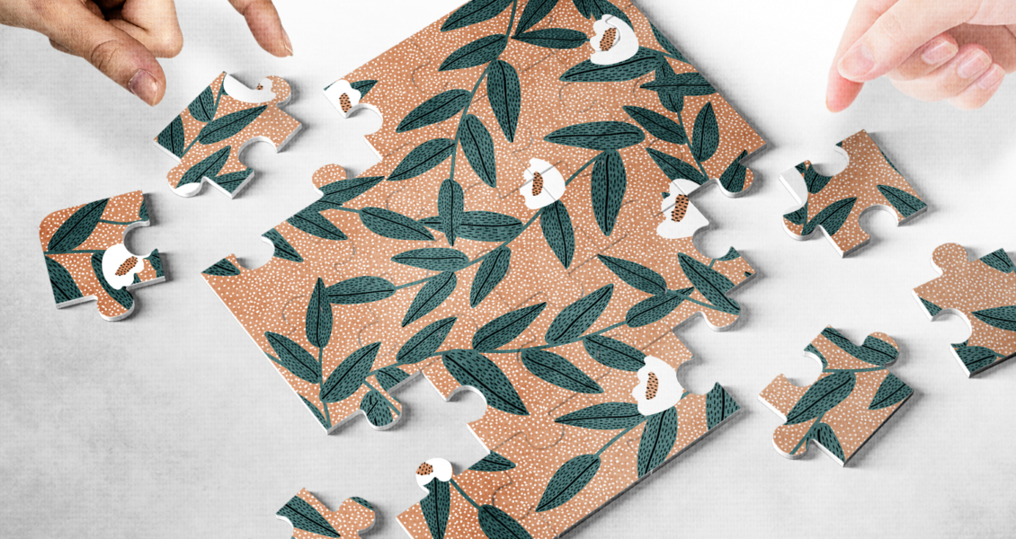 Hands assembling a floral-patterned jigsaw puzzle on a light surface.