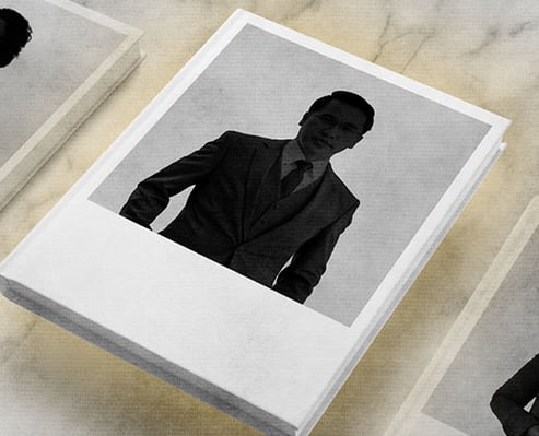 Black and white photograph of a man in a suit and tie on a stack of Polaroid-style pictures.